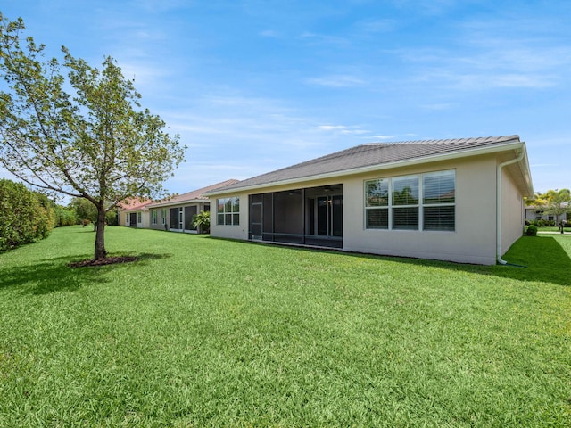 rear view of property featuring a sunroom, a tile roof, a yard, and stucco siding