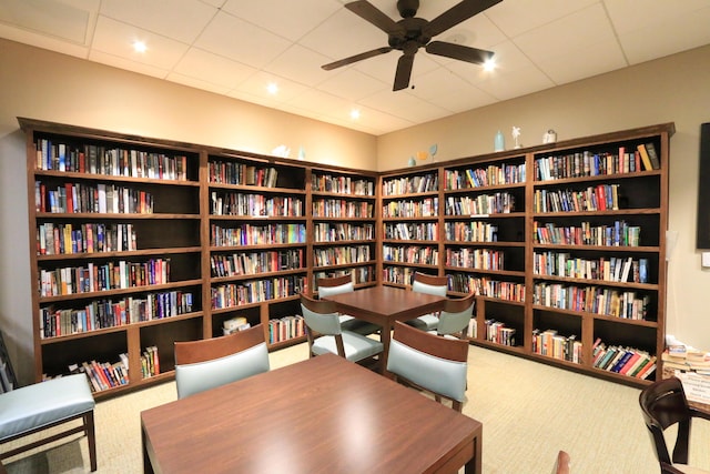 living area with carpet flooring, ceiling fan, and wall of books