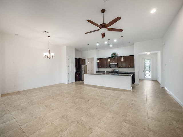 kitchen with appliances with stainless steel finishes, dark brown cabinets, ceiling fan with notable chandelier, pendant lighting, and a center island with sink