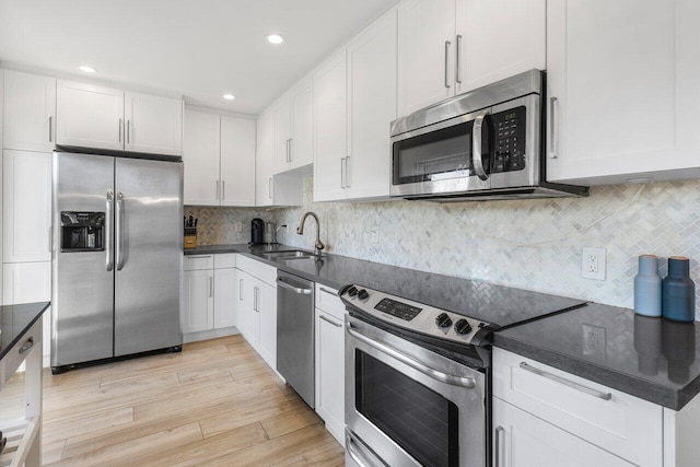 kitchen with dark countertops, appliances with stainless steel finishes, white cabinets, a sink, and light wood-type flooring