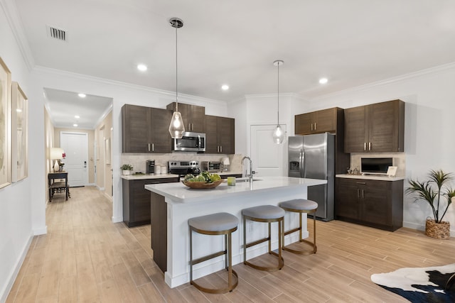 kitchen with dark brown cabinets, stainless steel appliances, sink, hanging light fixtures, and an island with sink