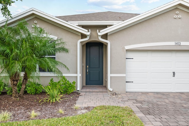 property entrance with a garage, a shingled roof, and stucco siding