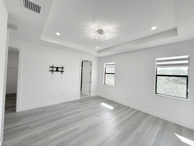 empty room featuring light wood-type flooring and a tray ceiling