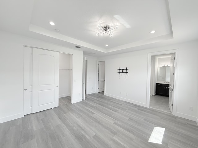 unfurnished bedroom with ensuite bathroom, a raised ceiling, and light wood-type flooring