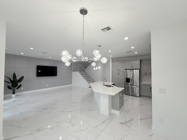 kitchen with gray cabinetry, sink, stainless steel refrigerator with ice dispenser, an island with sink, and pendant lighting