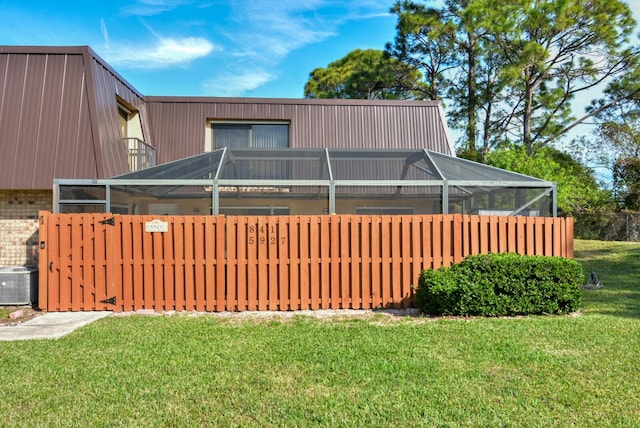 rear view of house featuring glass enclosure, central AC unit, and a lawn