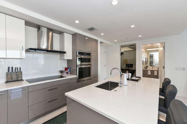 kitchen featuring a kitchen bar, a kitchen island with sink, sink, and wall chimney range hood