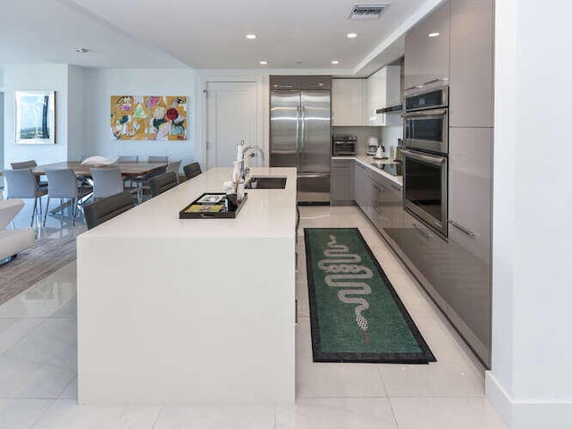 kitchen featuring sink, gray cabinets, a kitchen island with sink, light tile patterned floors, and appliances with stainless steel finishes