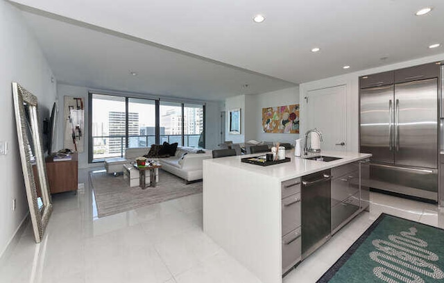 kitchen with a kitchen island with sink, sink, light tile patterned floors, dishwasher, and built in refrigerator