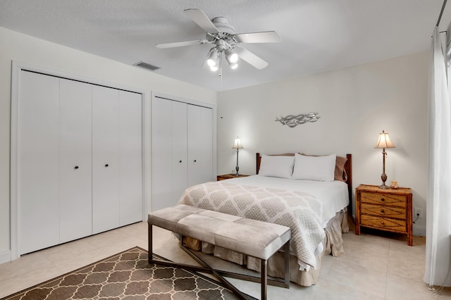 bedroom with ceiling fan, light tile patterned floors, a textured ceiling, and multiple closets