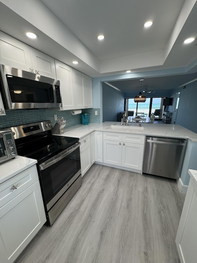 kitchen with kitchen peninsula, appliances with stainless steel finishes, backsplash, light hardwood / wood-style flooring, and white cabinetry