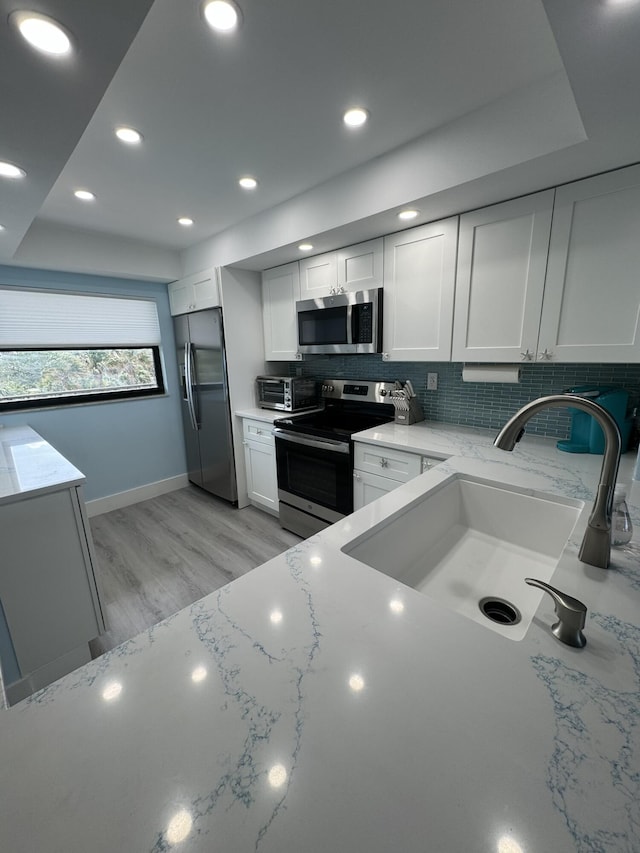 kitchen with backsplash, sink, appliances with stainless steel finishes, light hardwood / wood-style floors, and white cabinetry