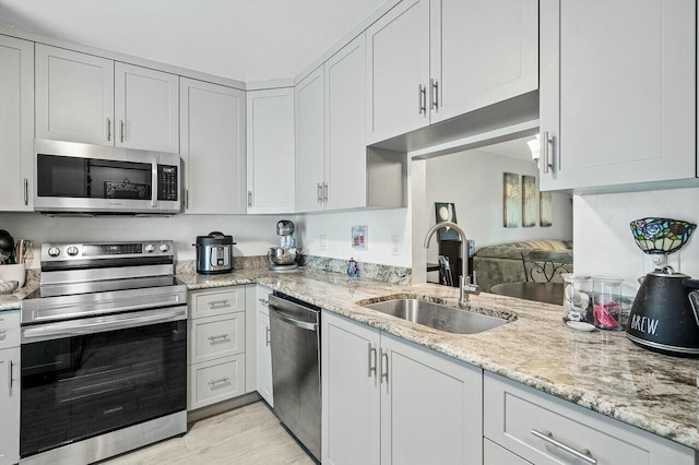 kitchen featuring light stone counters, stainless steel appliances, sink, light hardwood / wood-style flooring, and white cabinetry