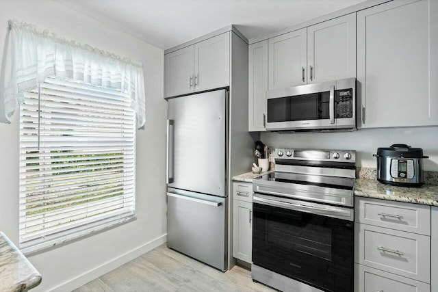 kitchen with gray cabinets, light stone countertops, light wood-type flooring, and stainless steel appliances