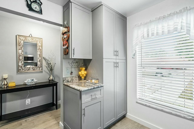 bar with gray cabinetry, light stone counters, a healthy amount of sunlight, and light hardwood / wood-style floors