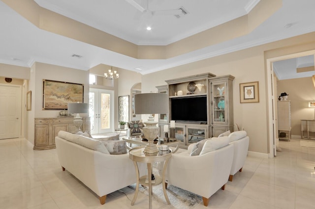 tiled living room featuring a tray ceiling, french doors, ceiling fan with notable chandelier, and ornamental molding