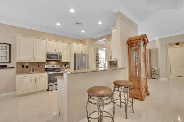 kitchen featuring a kitchen bar, appliances with stainless steel finishes, kitchen peninsula, light stone countertops, and ornamental molding