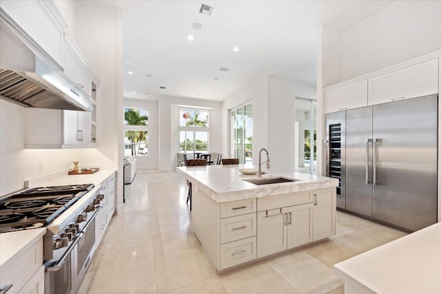 kitchen with sink, premium appliances, ventilation hood, a center island with sink, and light tile patterned floors