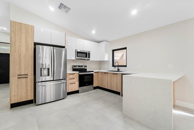 kitchen with appliances with stainless steel finishes, white cabinetry, lofted ceiling, and sink