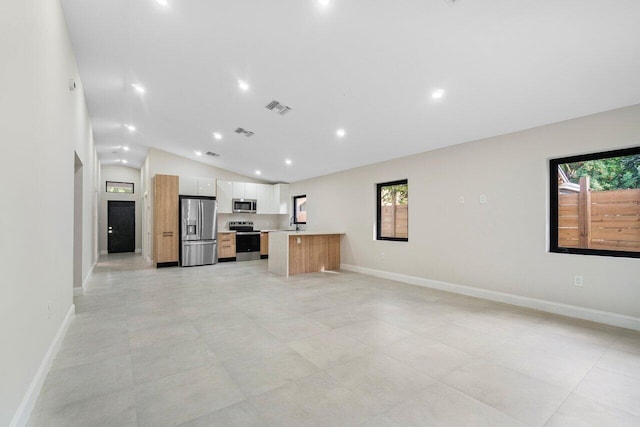 kitchen featuring a center island, lofted ceiling, sink, appliances with stainless steel finishes, and white cabinetry