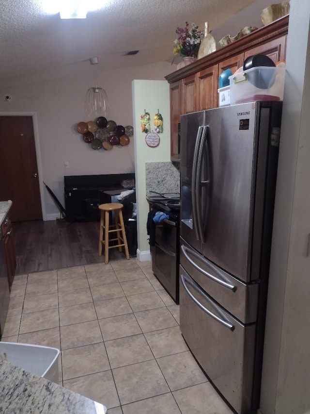 kitchen with light stone countertops, light tile patterned floors, a textured ceiling, and black appliances