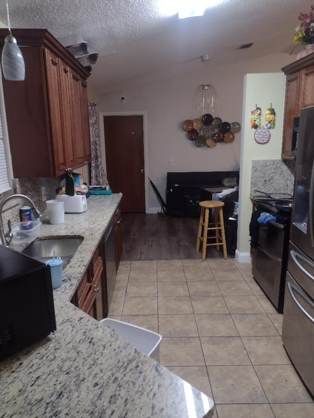 kitchen with light stone countertops, sink, tasteful backsplash, decorative light fixtures, and appliances with stainless steel finishes