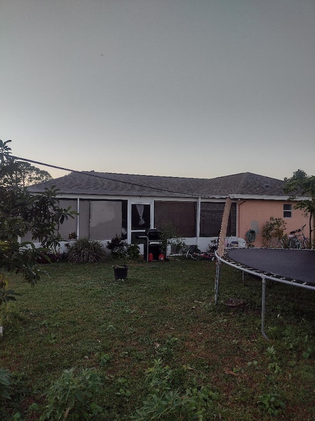 back house at dusk with a lawn and a trampoline