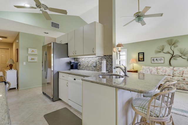 kitchen featuring lofted ceiling, white dishwasher, a kitchen breakfast bar, sink, and white cabinetry