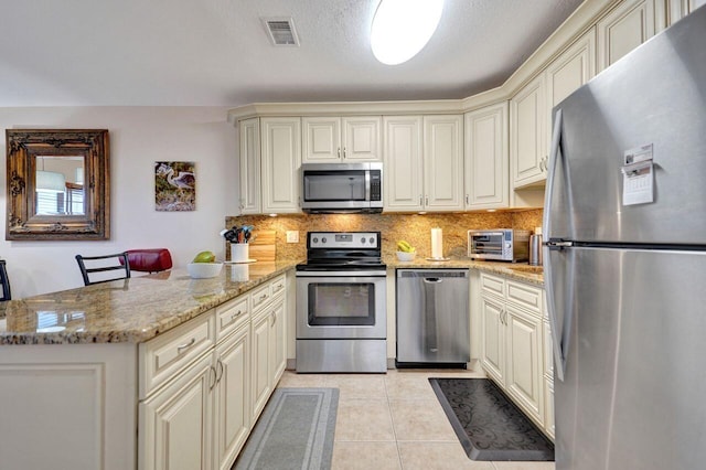 kitchen with cream cabinetry, stainless steel appliances, kitchen peninsula, and light stone countertops