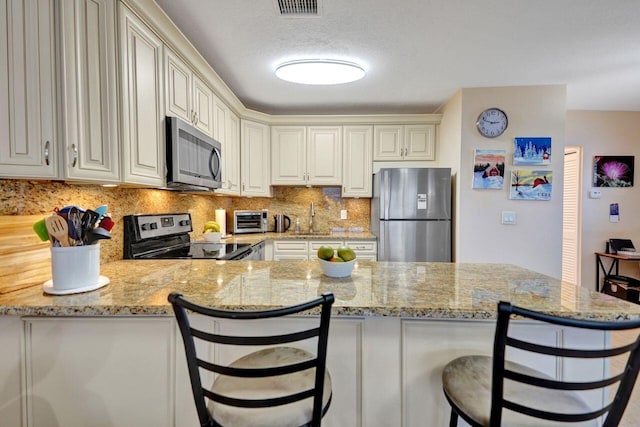 kitchen with a breakfast bar area, kitchen peninsula, light stone countertops, and stainless steel appliances