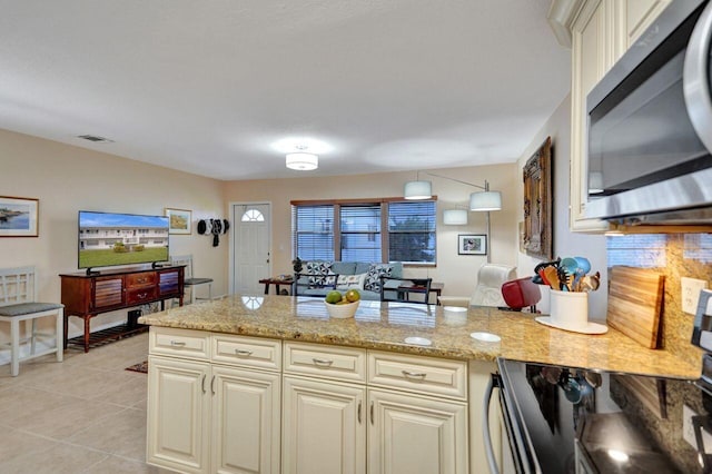 kitchen featuring cream cabinetry, stove, light stone countertops, and light tile patterned floors