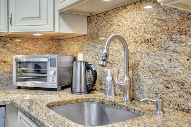 kitchen with white cabinets, tasteful backsplash, light stone countertops, and sink