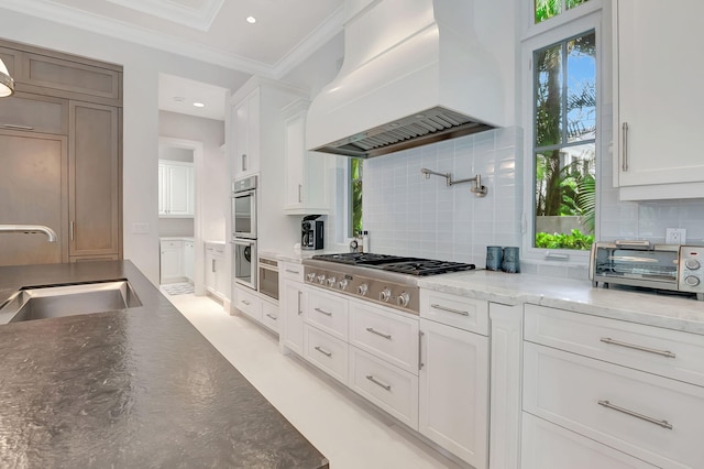 kitchen featuring white cabinets, custom range hood, decorative backsplash, and stainless steel appliances