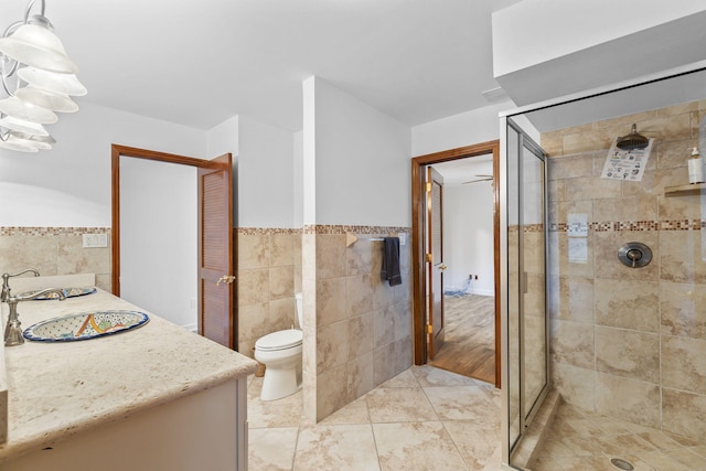 bathroom featuring a shower with door, vanity, tile walls, and toilet