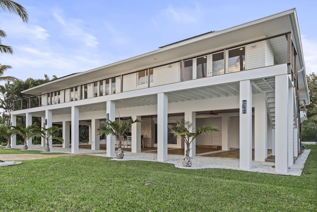 rear view of property with a balcony, ceiling fan, a patio area, and a lawn