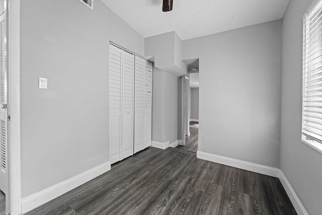 unfurnished bedroom with a closet, dark hardwood / wood-style floors, multiple windows, and ceiling fan