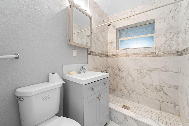 bathroom featuring a tile shower, vanity, a textured ceiling, and toilet