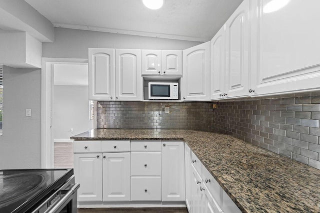 kitchen with tasteful backsplash, dark hardwood / wood-style floors, dark stone countertops, lofted ceiling, and white cabinets