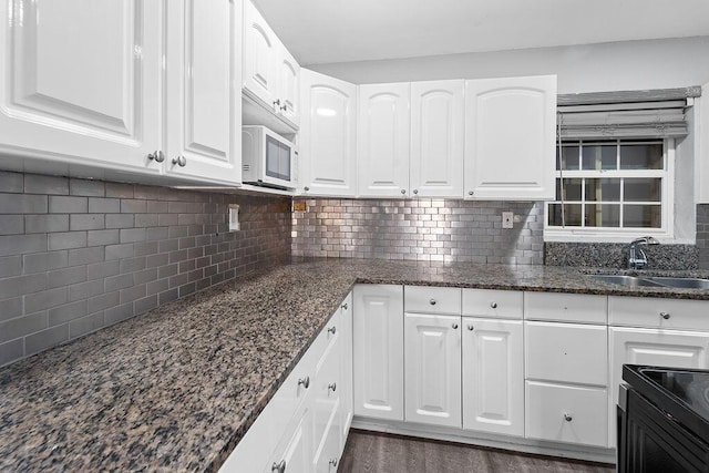 kitchen with dark stone countertops, white cabinetry, and sink