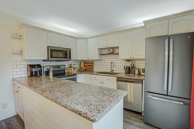 kitchen featuring light stone countertops, appliances with stainless steel finishes, kitchen peninsula, and sink