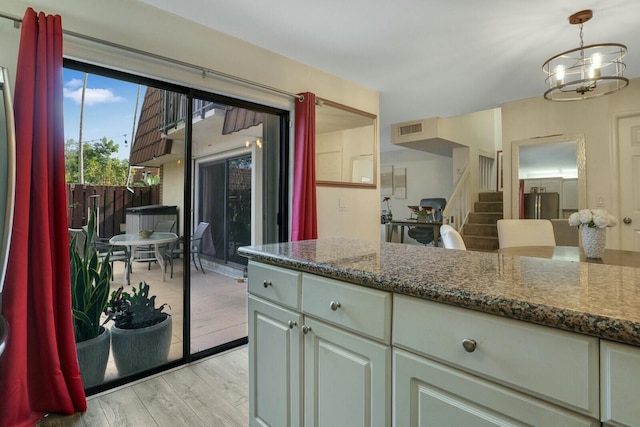 kitchen with decorative light fixtures, stainless steel fridge, light hardwood / wood-style flooring, and dark stone counters