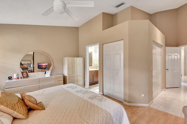 bedroom with a high ceiling, ensuite bathroom, light hardwood / wood-style flooring, ceiling fan, and a textured ceiling