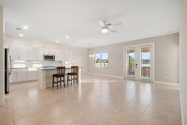 kitchen featuring white cabinetry, french doors, hanging light fixtures, an island with sink, and appliances with stainless steel finishes