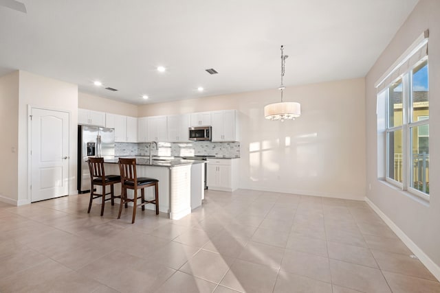 kitchen with pendant lighting, a center island with sink, decorative backsplash, white cabinetry, and stainless steel appliances