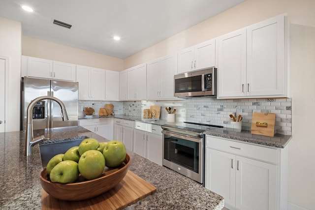 kitchen featuring white cabinetry, appliances with stainless steel finishes, and dark stone counters