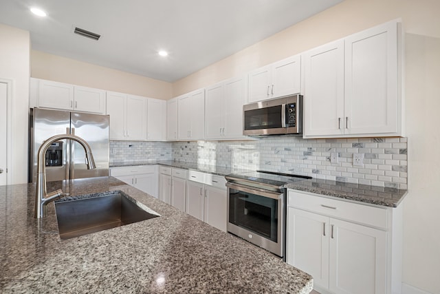 kitchen with appliances with stainless steel finishes, sink, white cabinetry, and dark stone countertops