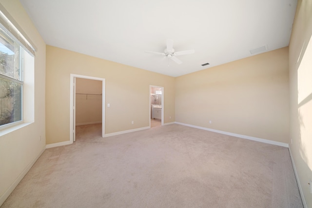 unfurnished bedroom with ceiling fan, ensuite bathroom, a walk in closet, light carpet, and a closet