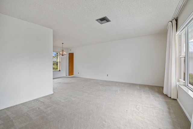 carpeted spare room featuring a textured ceiling and an inviting chandelier