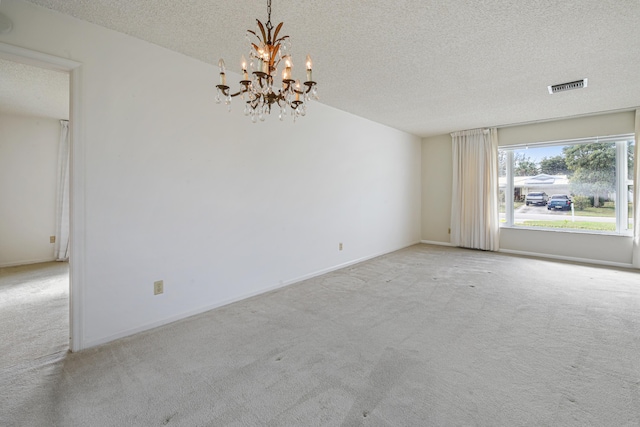 empty room with light carpet, a textured ceiling, and a notable chandelier