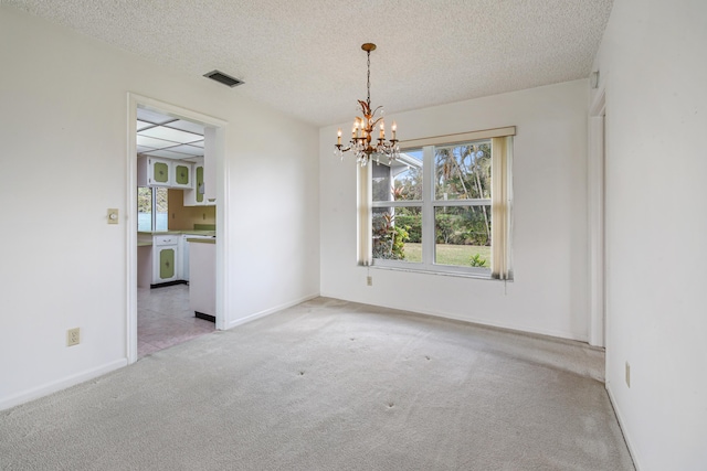 spare room featuring a notable chandelier, a textured ceiling, and light carpet